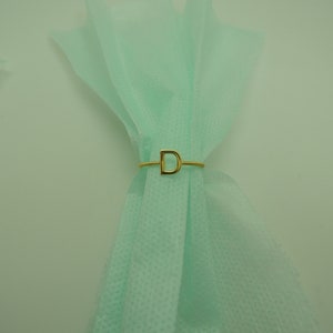 May include: A gold ring with the letter "D" on a light green fabric background.