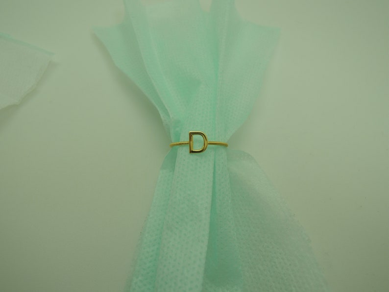 May include: A gold ring with the letter "D" on a light green fabric background.