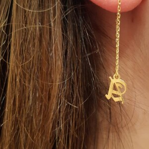 May include: Gold dangle earrings with a star charm and a letter 'A' charm hanging from a chain.