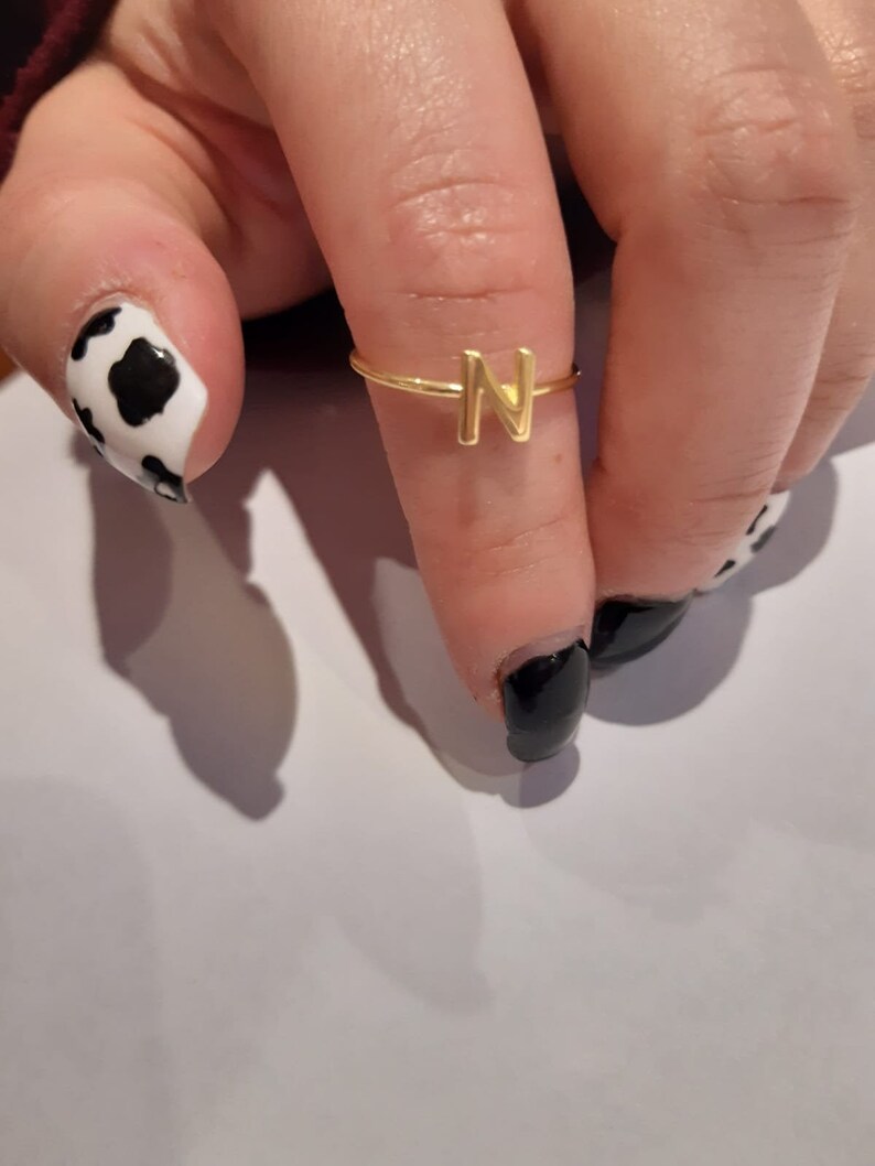 May include: A gold ring with the letter N on it. The ring is on a person's finger.