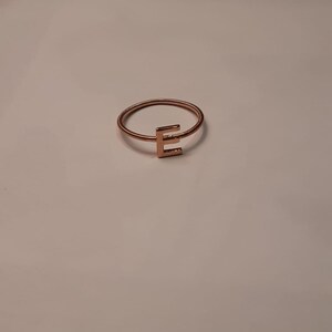 May include: A gold-toned ring with a simple, wire-like band and a letter 'E' charm.