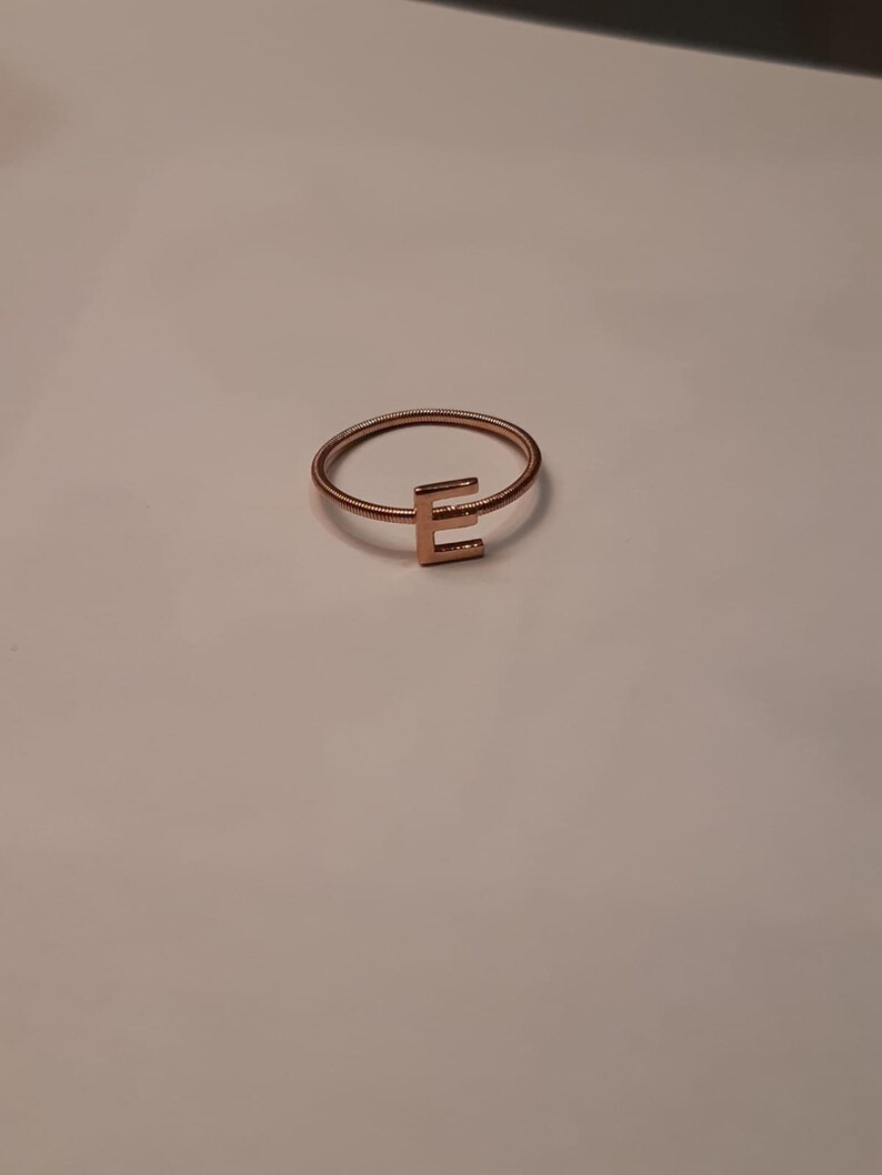 May include: A gold-toned ring with a simple, wire-like band and a letter 'E' charm.