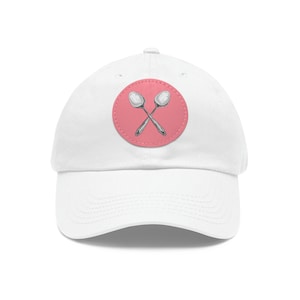 May include: White baseball cap with a pink circle patch featuring two crossed silver spoons.