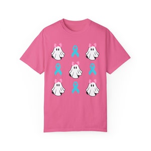 Puede incluir: Camiseta rosa con un patrón de fantasmas blancos que llevan lazos rosas y cintas azul claro.