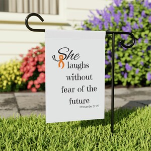 May include: A white garden flag with an orange ribbon and the text "She laughs without fear of the future Proverbs 31:25".