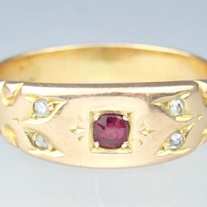 Puede incluir: Un anillo de oro con una piedra preciosa roja y pequeñas piedras blancas engastadas en un diseño decorativo.