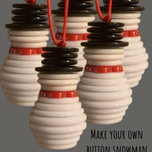 May include: Four white button snowmen ornaments with red and black buttons. The snowmen are hanging from red string. The text "MAKE YOUR OWN BUTTON SNOWMAN 16 BUTTONS" is at the bottom of the image.
