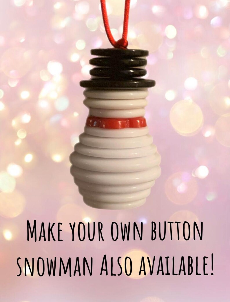 May include: A white button snowman ornament with a red hat and black button eyes. The snowman is hanging from a red string. The text "MAKE YOUR OWN BUTTON SNOWMAN ALSO AVAILABLE!" is at the bottom of the image.