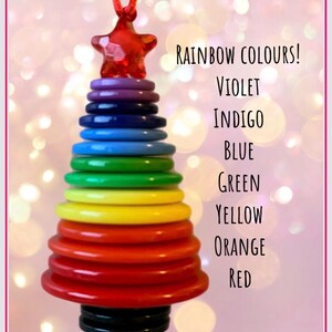 May include: A rainbow-colored Christmas tree ornament made of stacked plastic rings. The ornament is hung from a red string and has a star-shaped topper. The colors of the rings are red, orange, yellow, green, blue, indigo, and violet. The text "RAINBOW COLOURS!" is written above the ornament, followed by the colors of the rings in descending order.