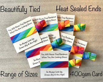 May include: Assortment of rainbow-colored elastic hair ties with inspirational messages printed on white cards. The messages include "You Will Never Find Rainbows When You Are Looking Down" and "So Always Look Up, Dream Big & Aim High!" The hair ties are made with 400gsm card.