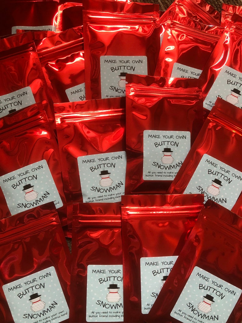 May include: Multiple red zippered bags with white labels that say "Make Your Own Button Snowman". The labels have a snowman illustration and instructions on how to make a button snowman.