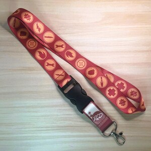 May include: A red lanyard with a repeating pattern of orange circular icons. The lanyard has a black plastic clasp and a metal clip. The text "RED" is visible on the bottom of the lanyard.