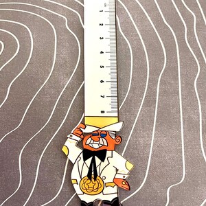 May include: A white ruler with black markings up to 8 cm, attached to a cartoon character wearing a white suit, yellow hat, and a black bow tie. The character is holding a gold star medal.