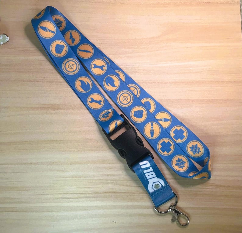 May include: Blue lanyard with repeating orange and yellow circular designs. The lanyard has a black plastic clasp and a metal clip. The text "BLU" and a wrench graphic are printed on the bottom portion of the lanyard.