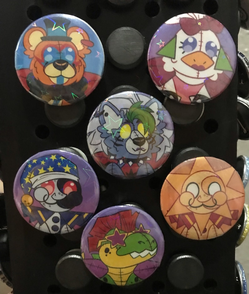 Puede incluir: Seis botones redondos de colores con diferentes personajes de dibujos animados. Los botones presentan un oso con un sombrero de copa, una gallina con un lazo rojo, un lobo con pelo verde, un buf&oacute;n con un sombrero morado, un sol sonriente y un dinosaurio con un mohawk verde.
