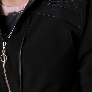 Puede incluir: Una chaqueta negra con cierre de cremallera y cuello de imitaci&oacute;n de cuero. El cuello tiene un dise&ntilde;o texturizado.