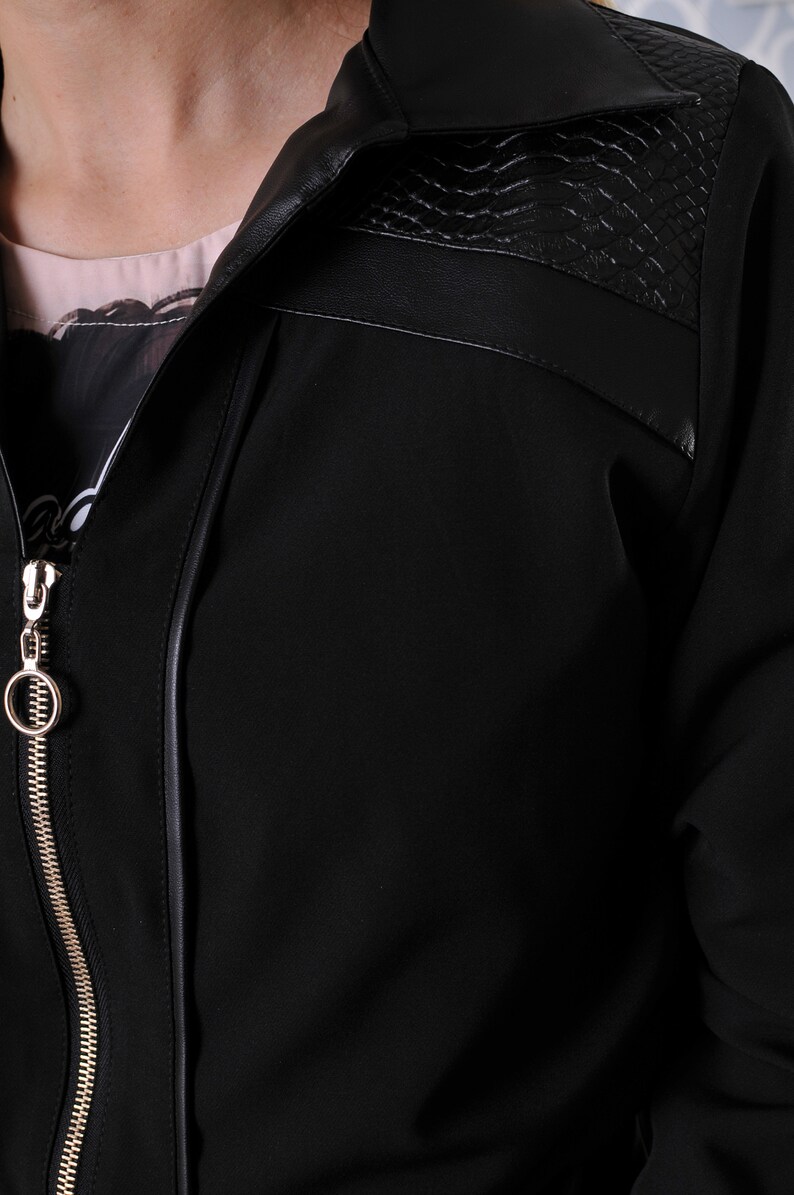 Puede incluir: Una chaqueta negra con cierre de cremallera y cuello de imitaci&oacute;n de cuero. El cuello tiene un dise&ntilde;o texturizado.