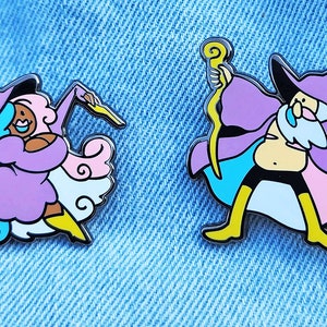 May include: Two enamel pins depicting cartoon wizards. One wizard is female with pink and blue hair, wearing a purple robe and holding a wand. The other wizard is male with a white beard, wearing a purple robe and holding a staff. Both pins have a yellow outline.