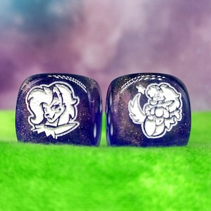 May include: Two purple dice with white illustrations of cartoon characters. The dice are on a green surface.