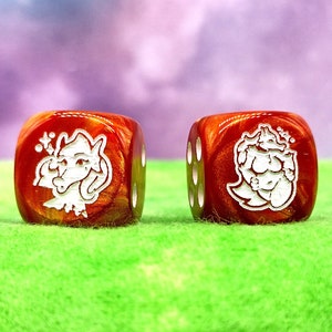 May include: Two red dice with white designs. The dice have a cartoon-like image of a creature with a crown on its head.
