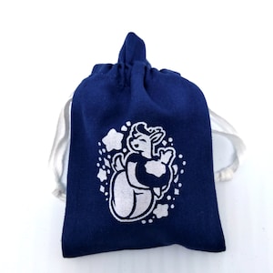 May include: A small blue drawstring bag with a white design of a cartoon animal holding a soccer ball. The design is surrounded by white stars.
