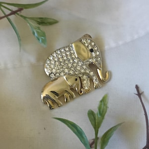 Puede incluir: Un broche de elefante dorado con diamantes de imitación, que representa a una madre elefante y a un bebé elefante.