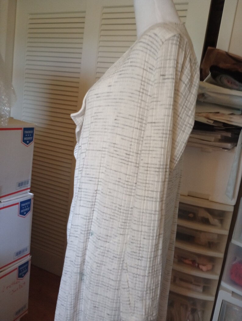 May include: A white long-sleeved cardigan with a subtle gray striped pattern. The cardigan has a V-neck and a relaxed fit.