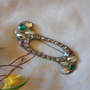 May include: A gold-toned brooch with a unique shape and a variety of colorful rhinestones, including green, red, and white.