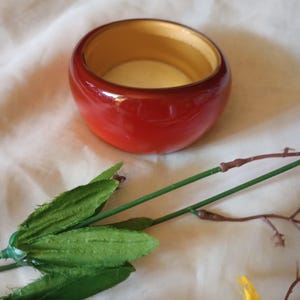 May include: A red and brown wooden bangle bracelet with a smooth, glossy finish.