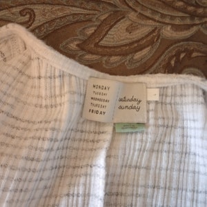 May include: White ribbed knit top with a white tag that says "Monday, Tuesday, Wednesday, Thursday, Friday, Saturday, Sunday".