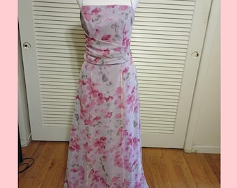 May include: A light purple floral print dress with spaghetti straps. The dress features a fitted bodice and a flowing skirt. Pink and purple flowers are scattered across the fabric. The dress is displayed on a mannequin.