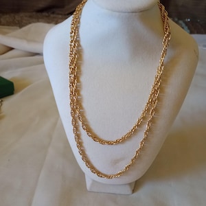 Pode incluir: Um colar de corrente dourado com um design de corda. O colar é exibido em um busto de manequim branco.