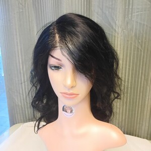 May include: A black, wavy wig styled on a mannequin head. The wig features a side part and shoulder-length layers. The mannequin has a fair complexion and is set against a light background.