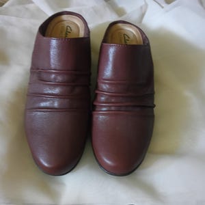 Puede incluir: Un par de zapatos marrones de cuero con un diseño simple y un dedo del pie ligeramente redondeado. Los zapatos están hechos de cuero suave y flexible. El nombre de la marca "Clarks Collection" es visible en el interior de los zapatos.