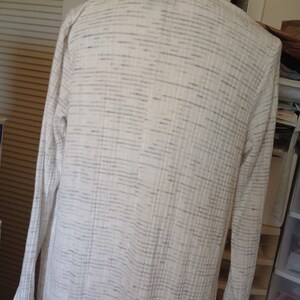 May include: A white cardigan with a subtle gray stripe pattern. The cardigan has long sleeves and a relaxed fit.