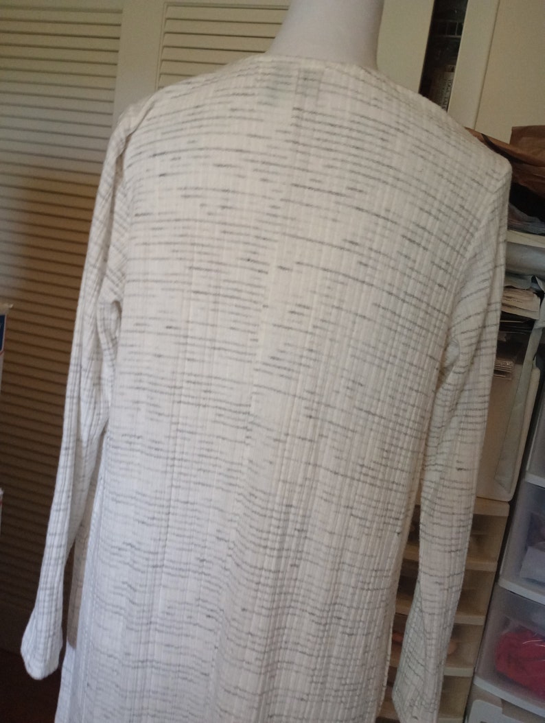 May include: A white cardigan with a subtle gray stripe pattern. The cardigan has long sleeves and a relaxed fit.