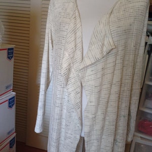 May include: A long white cardigan with a black and white striped pattern. The cardigan has a deep V-neck and is open in the front.