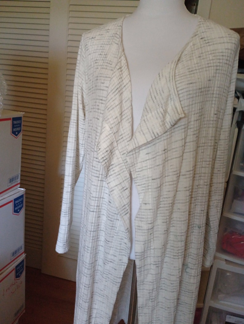 May include: A long white cardigan with a black and white striped pattern. The cardigan has a deep V-neck and is open in the front.