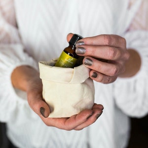 May include: A small, off-white leather pouch holds a brown essential oil bottle with a black cap. The bottle has a green and yellow label that reads "Lemongrass". The pouch is held in both hands against a soft, white background.