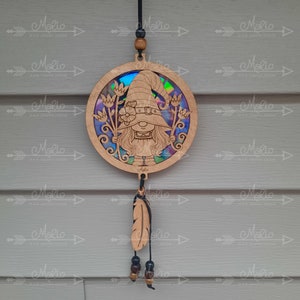 May include: A wooden gnome ornament with a rainbow iridescent background. The gnome is wearing a pointed hat and holding flowers. The ornament is hanging from a black cord with a wooden bead and a feather charm.