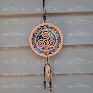 Può includere: Un acchiappasogni in legno con un design a tripla spirale e accenti iridescenti. L'acchiappasogni è appeso a un cordoncino nero con perline e una piuma marrone.