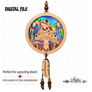 May include: A circular wooden laser-cut hanging ornament featuring a frog sitting on a mushroom, surrounded by flowers and smaller mushrooms. The center has an iridescent finish. Text reads DIGITAL FILE, Perfect for upcycling discs!, FOR LASER CUTTING & ENGRAVING, and Marlo.