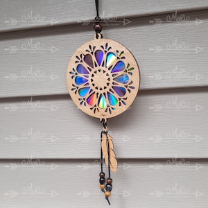 May include: A wooden dreamcatcher with a circular design featuring a holographic iridescent center. The dreamcatcher has a black cord and a brown feather with black beads hanging from it.