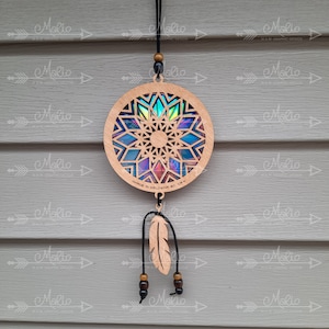 May include: A wooden dreamcatcher with a colorful iridescent center and a black leather cord. The dreamcatcher has a small wooden feather hanging from it and is made in Kelowna, BC, Canada.
