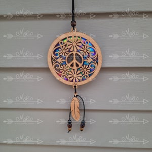 May include: A wooden peace sign ornament with a colorful iridescent background and floral designs. The ornament is hanging from a black cord with a brown feather and beads.