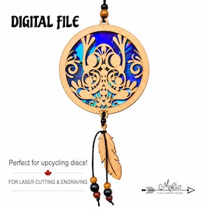 May include: A circular wooden cutout featuring an intricate frog design with a blue iridescent background. The piece includes a hanging black cord with wooden beads and a wooden feather charm. Text reads: DIGITAL FILE, Perfect for upcycling discs!, FOR LASER CUTTING & ENGRAVING, and Marlo MAM GRAPHIC DESIGN.