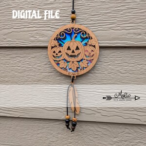 May include: A circular wooden hanging ornament featuring three carved jack-o'-lantern pumpkins with leaves, set against a blue iridescent background. The text DIGITAL FILE appears at the top, and a wooden feather charm hangs below with black beads.