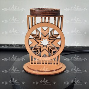 K&ouml;nnte beinhalten: Ein lasergeschnittener Kerzenhalter aus Holz mit einem kreisf&ouml;rmigen Rahmen und einem geometrischen Sternmuster in der Mitte. Die Struktur hat eine hellbraune Naturholzoberfl&auml;che mit dunkler gebeizten Kanten, einen flachen runden Sockel und einen oberen Ring.