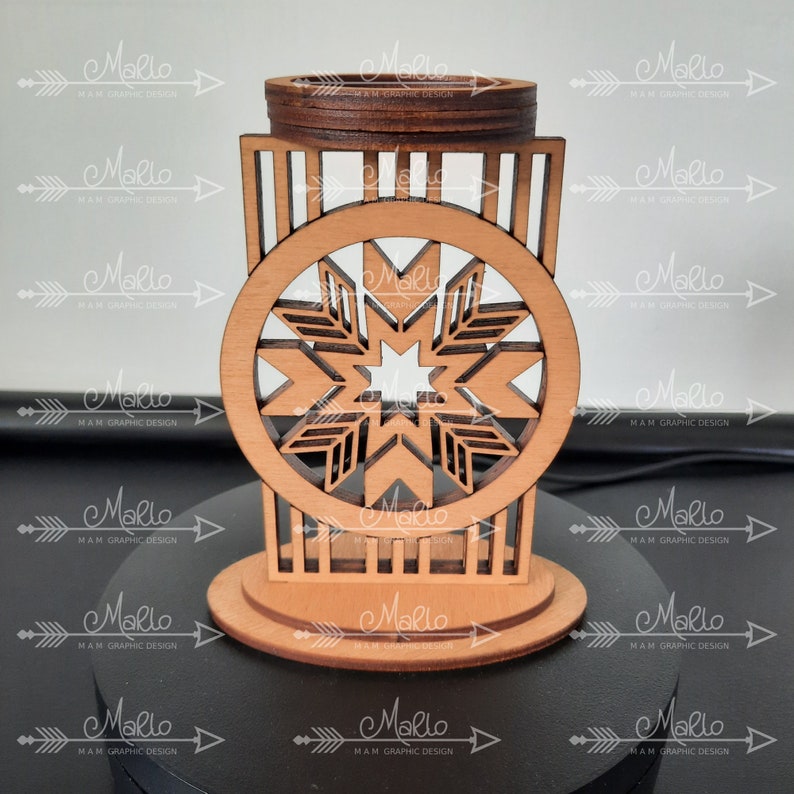 K&ouml;nnte beinhalten: Ein lasergeschnittener Kerzenhalter aus Holz mit einem kreisf&ouml;rmigen Rahmen und einem geometrischen Sternmuster in der Mitte. Die Struktur hat eine hellbraune Naturholzoberfl&auml;che mit dunkler gebeizten Kanten, einen flachen runden Sockel und einen oberen Ring.