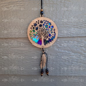 May include: A wooden tree of life ornament with iridescent leaves and a feather charm. The ornament is hanging from a black cord with wooden beads.